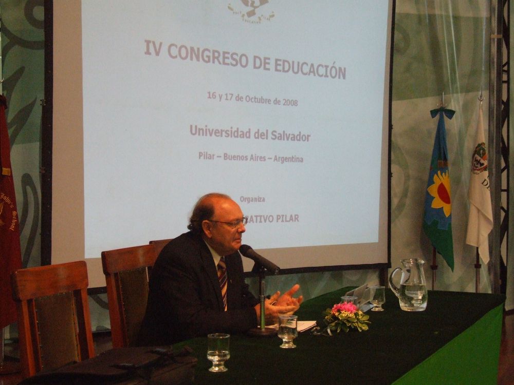 Un orador sentado a la mesa, junto a la pantalla del IV Congreso de Educación, el 16 y 17 de octubre de 2008