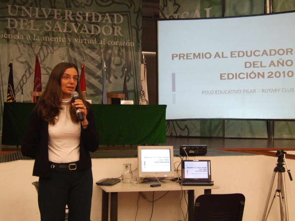 Una docente habla con el micrófono frente a la pantalla del Premio al Educador del Año, edición 2010