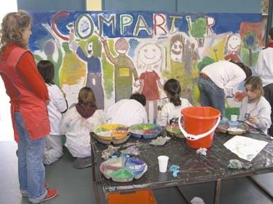 Alumnos de guardapolvo blanco pintan un mural con la palabra Compartir